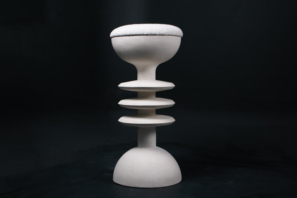 The Annulet barstool in white. The sculptural base rises from a domed foot through three stacked horizontal discs, narrowing to a stem that supports a wide chalice-shaped seat cradle, topped with a round white bouclé upholstered seat.
