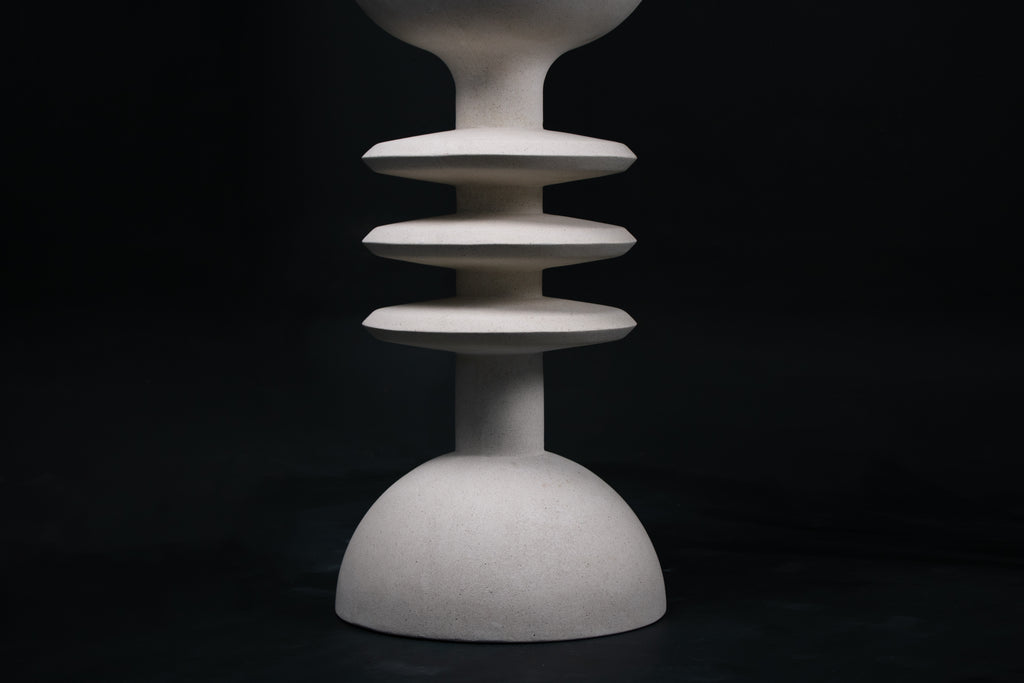 The Annulet barstool in white. The sculptural base rises from a domed foot through three stacked horizontal discs, narrowing to a stem that supports a wide chalice-shaped seat cradle, topped with a round white bouclé upholstered seat.