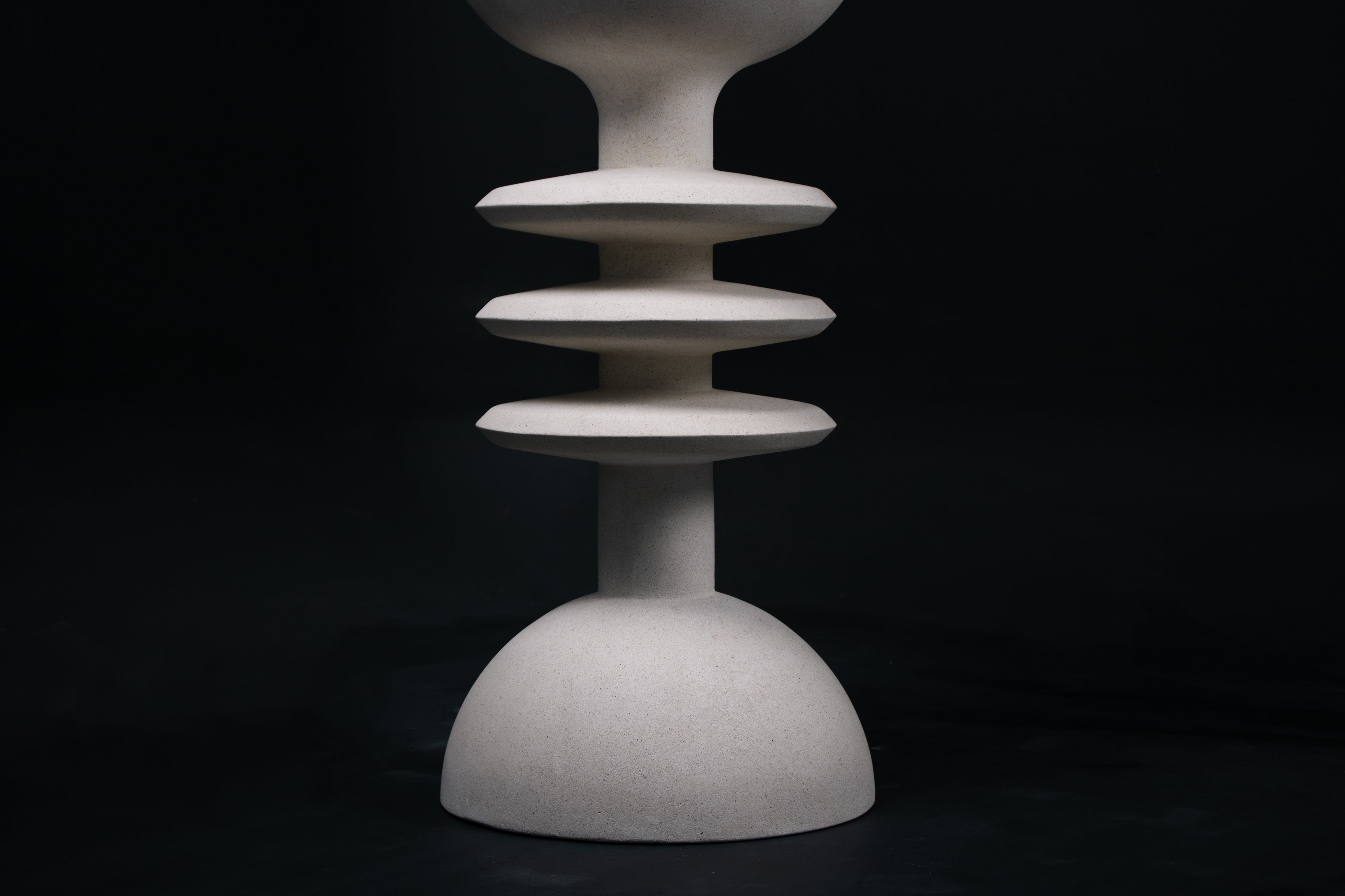 The Annulet barstool in white. The sculptural base rises from a domed foot through three stacked horizontal discs, narrowing to a stem that supports a wide chalice-shaped seat cradle, topped with a round white bouclé upholstered seat.