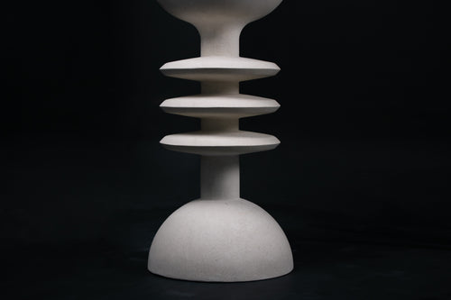 The Annulet barstool in white. The sculptural base rises from a domed foot through three stacked horizontal discs, narrowing to a stem that supports a wide chalice-shaped seat cradle, topped with a round white bouclé upholstered seat.