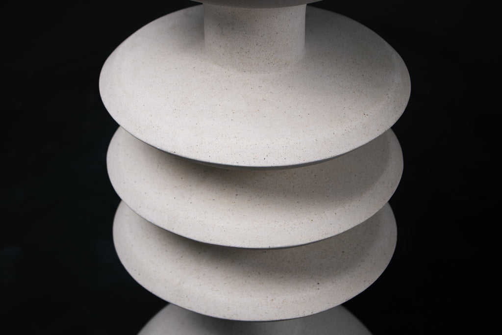 The Annulet barstool in white. The sculptural base rises from a domed foot through three stacked horizontal discs, narrowing to a stem that supports a wide chalice-shaped seat cradle, topped with a round white bouclé upholstered seat.
