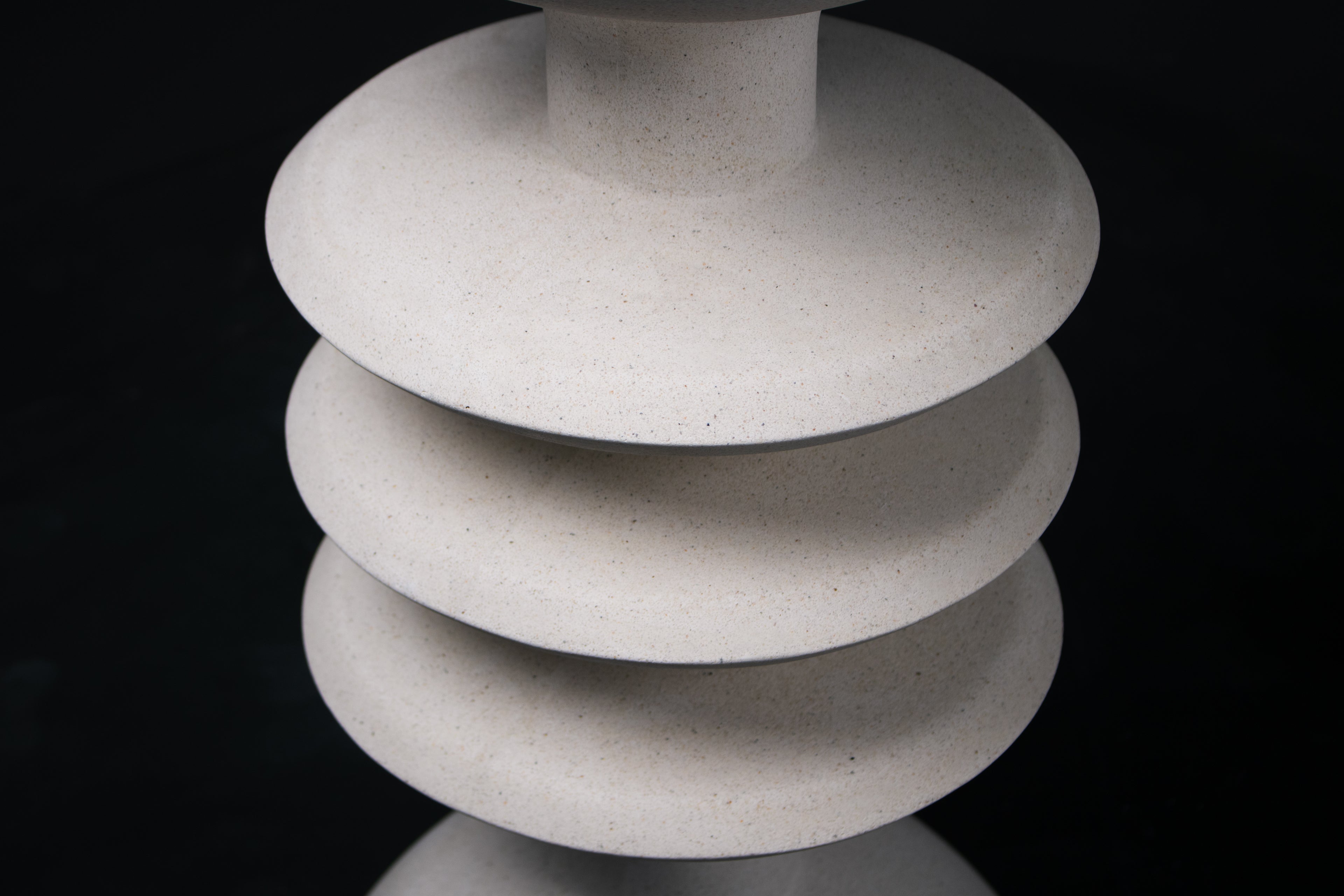 The Annulet barstool in white. The sculptural base rises from a domed foot through three stacked horizontal discs, narrowing to a stem that supports a wide chalice-shaped seat cradle, topped with a round white bouclé upholstered seat.
