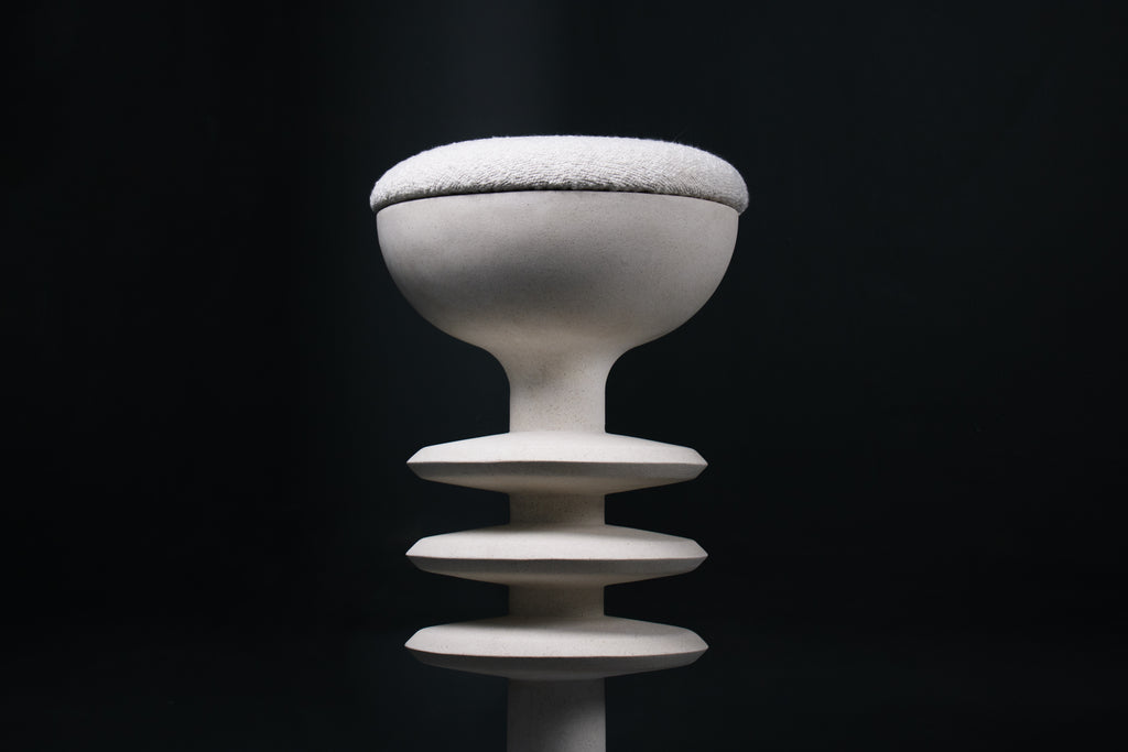 The Annulet barstool in white. The sculptural base rises from a domed foot through three stacked horizontal discs, narrowing to a stem that supports a wide chalice-shaped seat cradle, topped with a round white bouclé upholstered seat.