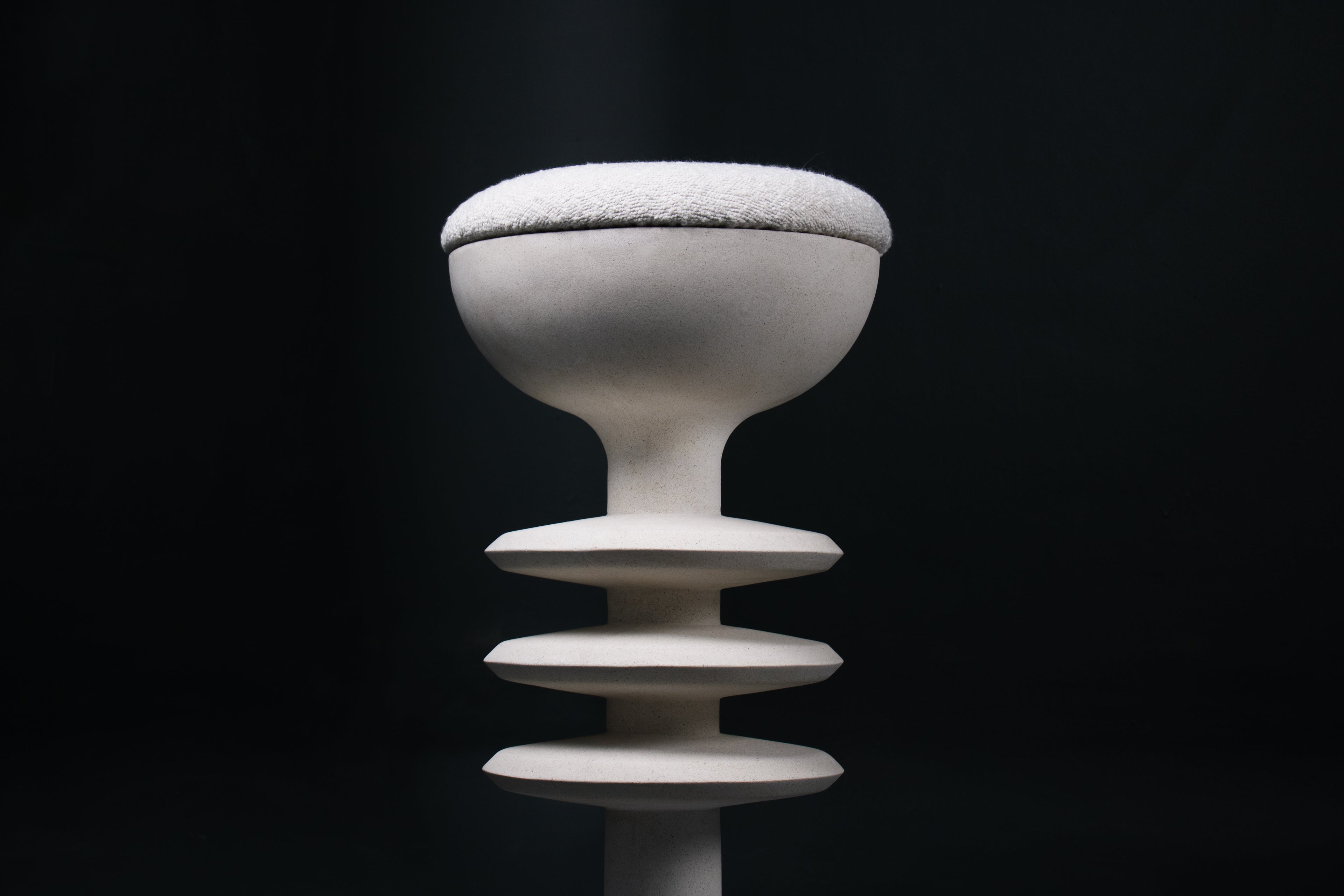 The Annulet barstool in white. The sculptural base rises from a domed foot through three stacked horizontal discs, narrowing to a stem that supports a wide chalice-shaped seat cradle, topped with a round white bouclé upholstered seat.