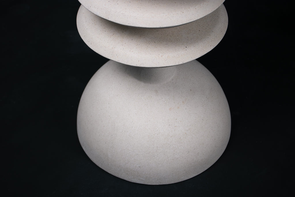 The Annulet barstool in white. The sculptural base rises from a domed foot through three stacked horizontal discs, narrowing to a stem that supports a wide chalice-shaped seat cradle, topped with a round white bouclé upholstered seat.