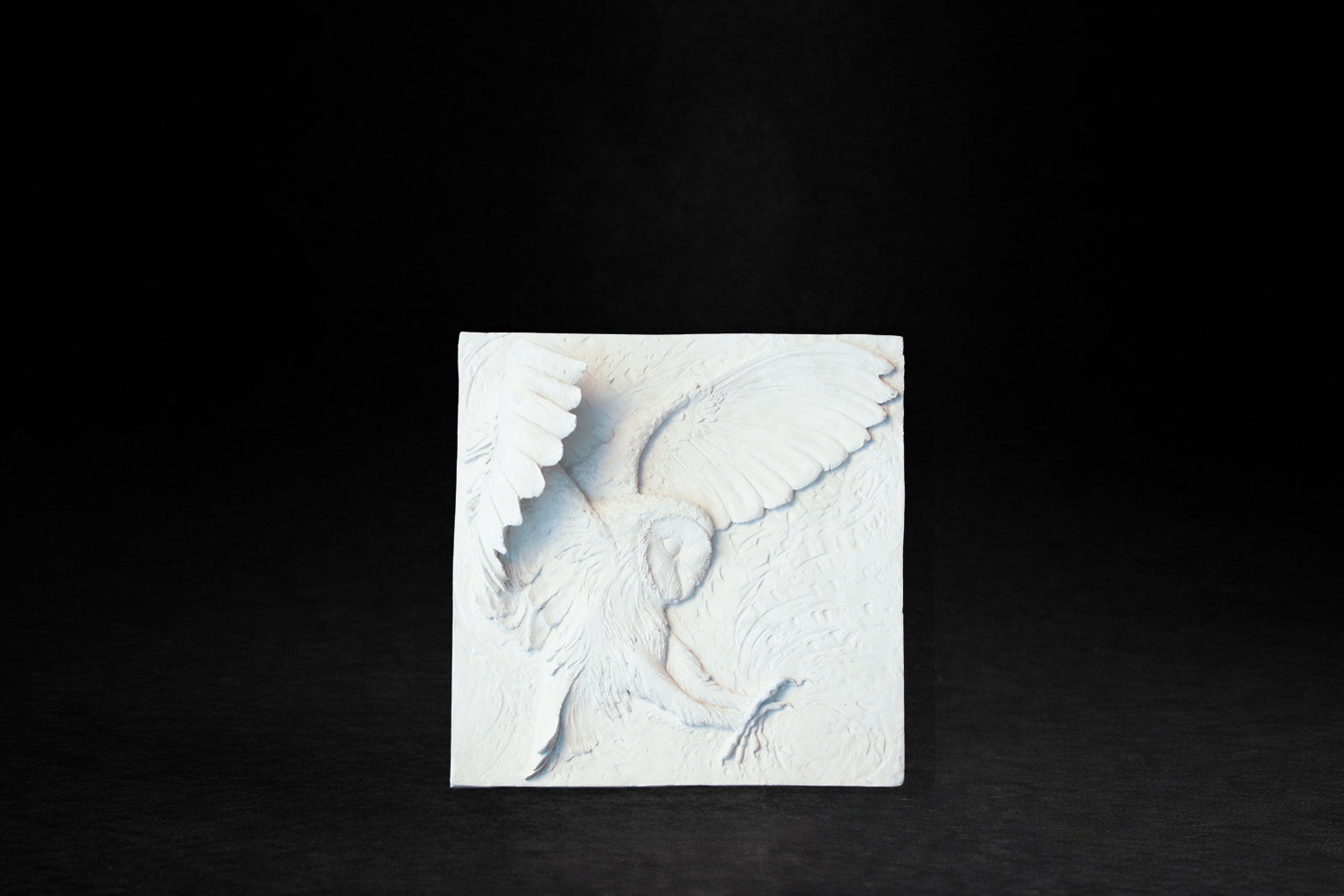 White plaster relief panel depicting a barn owl with wings fully spread in a hunting swoop.