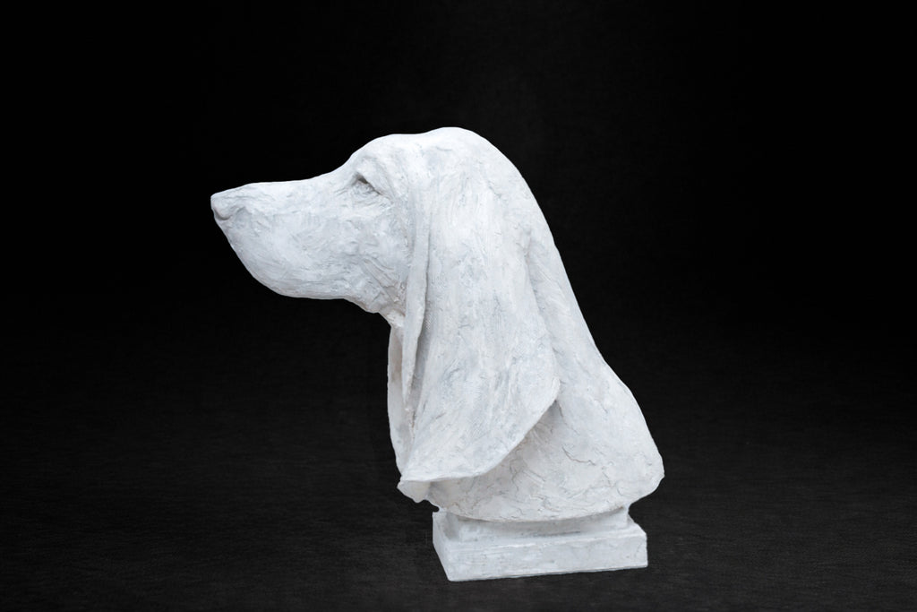 White plaster portrait bust of a Basset Hound with long drooping ears on a stepped square base.