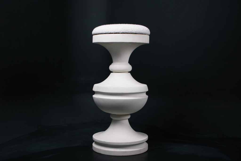 Chalice barstool in white. The substantial turned base draws on classical column and urn forms, a layered circular foot rises through a bulbous lower body, pinches to a narrow waist, then flares outward to support a round white bouclé upholstered seat.