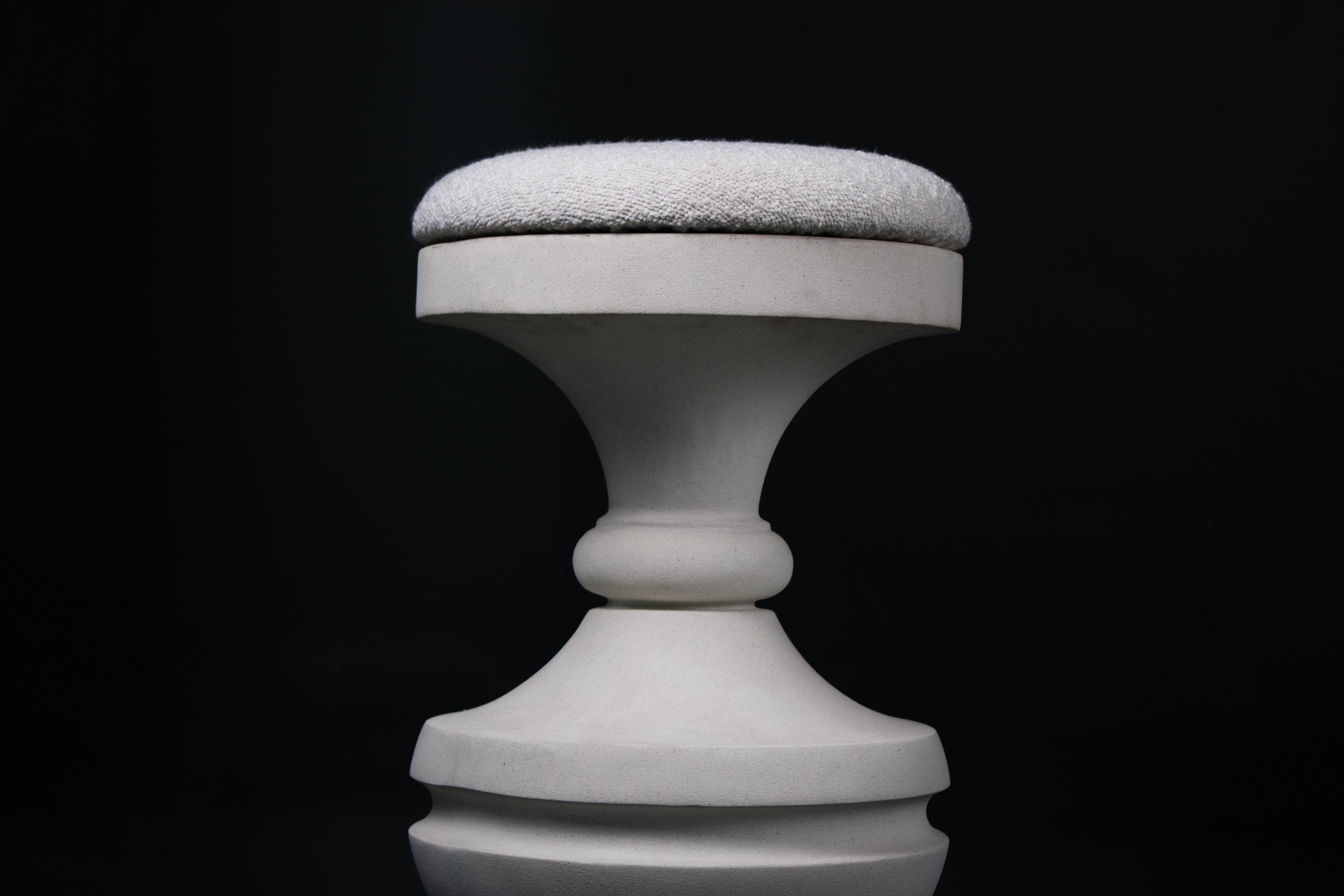 Chalice barstool in white. The substantial turned base draws on classical column and urn forms, a layered circular foot rises through a bulbous lower body, pinches to a narrow waist, then flares outward to support a round white bouclé upholstered seat.