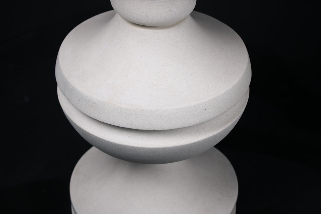 Chalice barstool in white. The substantial turned base draws on classical column and urn forms, a layered circular foot rises through a bulbous lower body, pinches to a narrow waist, then flares outward to support a round white bouclé upholstered seat.