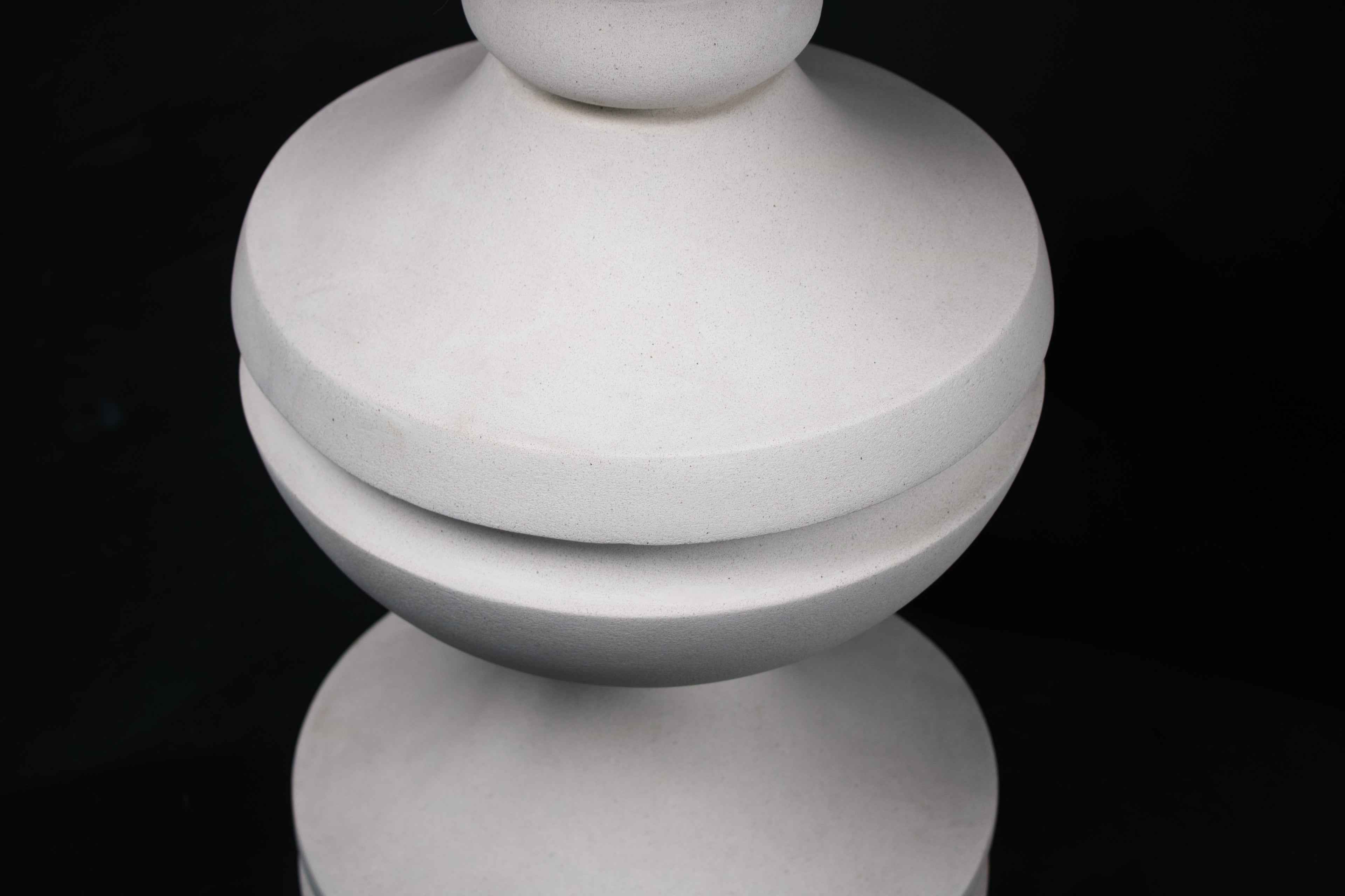 Chalice barstool in white. The substantial turned base draws on classical column and urn forms, a layered circular foot rises through a bulbous lower body, pinches to a narrow waist, then flares outward to support a round white bouclé upholstered seat.