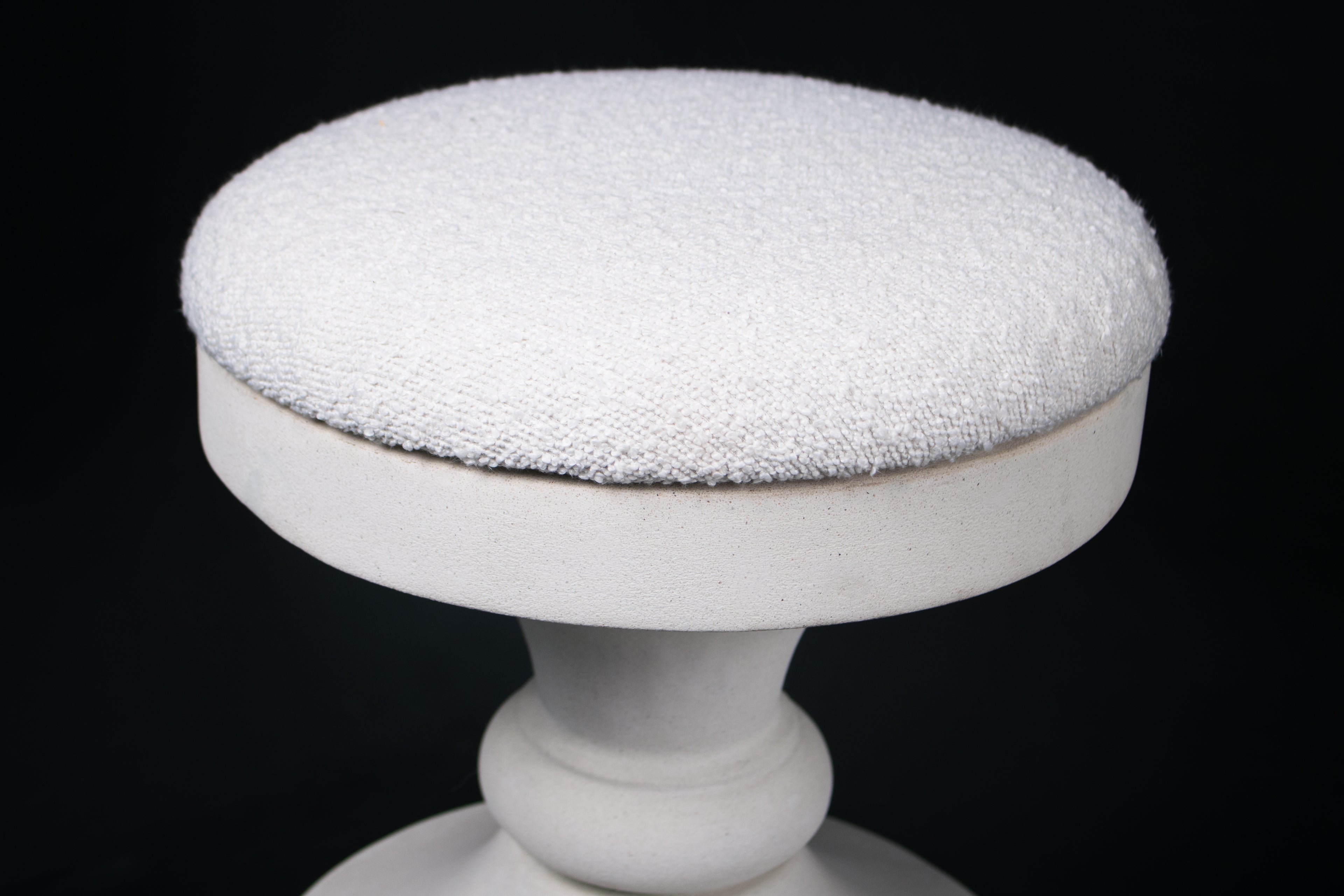 Chalice barstool in white. The substantial turned base draws on classical column and urn forms, a layered circular foot rises through a bulbous lower body, pinches to a narrow waist, then flares outward to support a round white bouclé upholstered seat.
