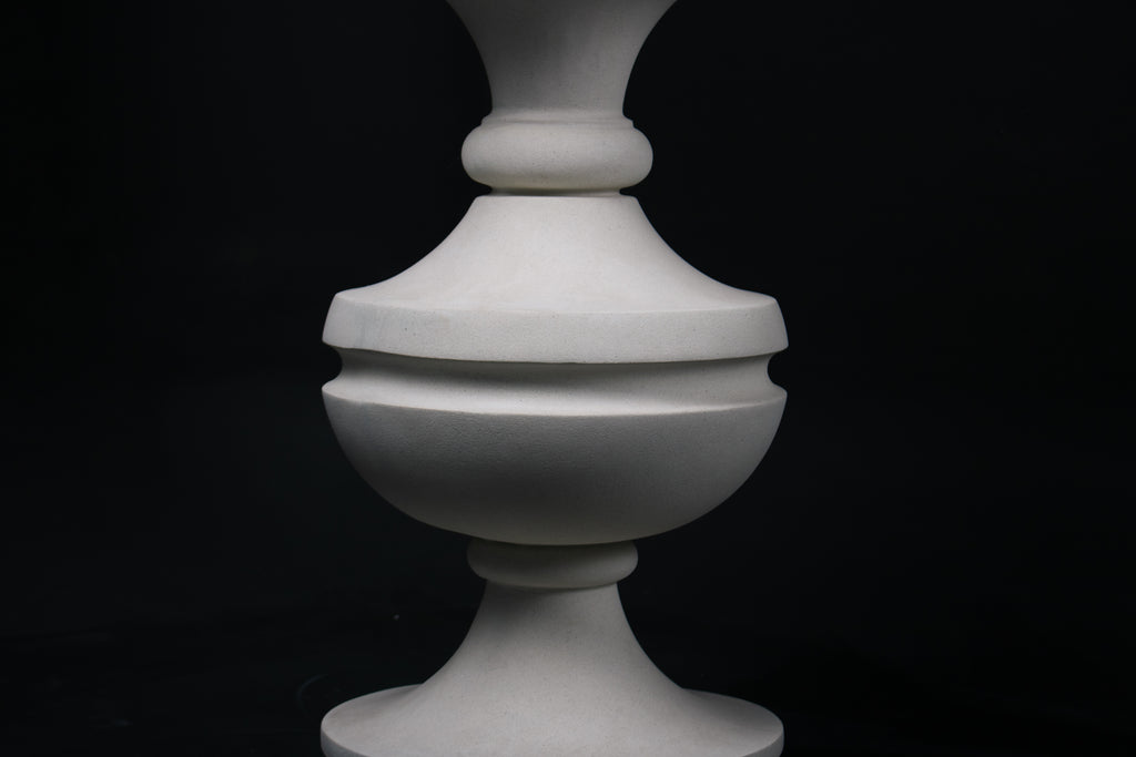 Chalice barstool in white. The substantial turned base draws on classical column and urn forms, a layered circular foot rises through a bulbous lower body, pinches to a narrow waist, then flares outward to support a round white bouclé upholstered seat.