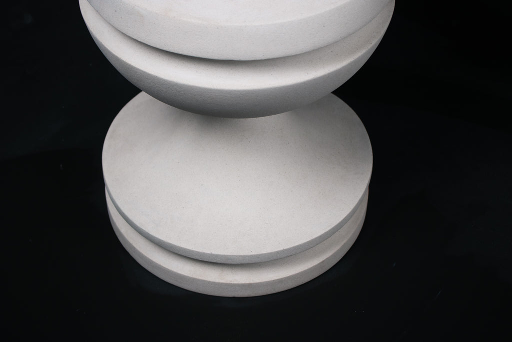 Chalice barstool in white. The substantial turned base draws on classical column and urn forms, a layered circular foot rises through a bulbous lower body, pinches to a narrow waist, then flares outward to support a round white bouclé upholstered seat.