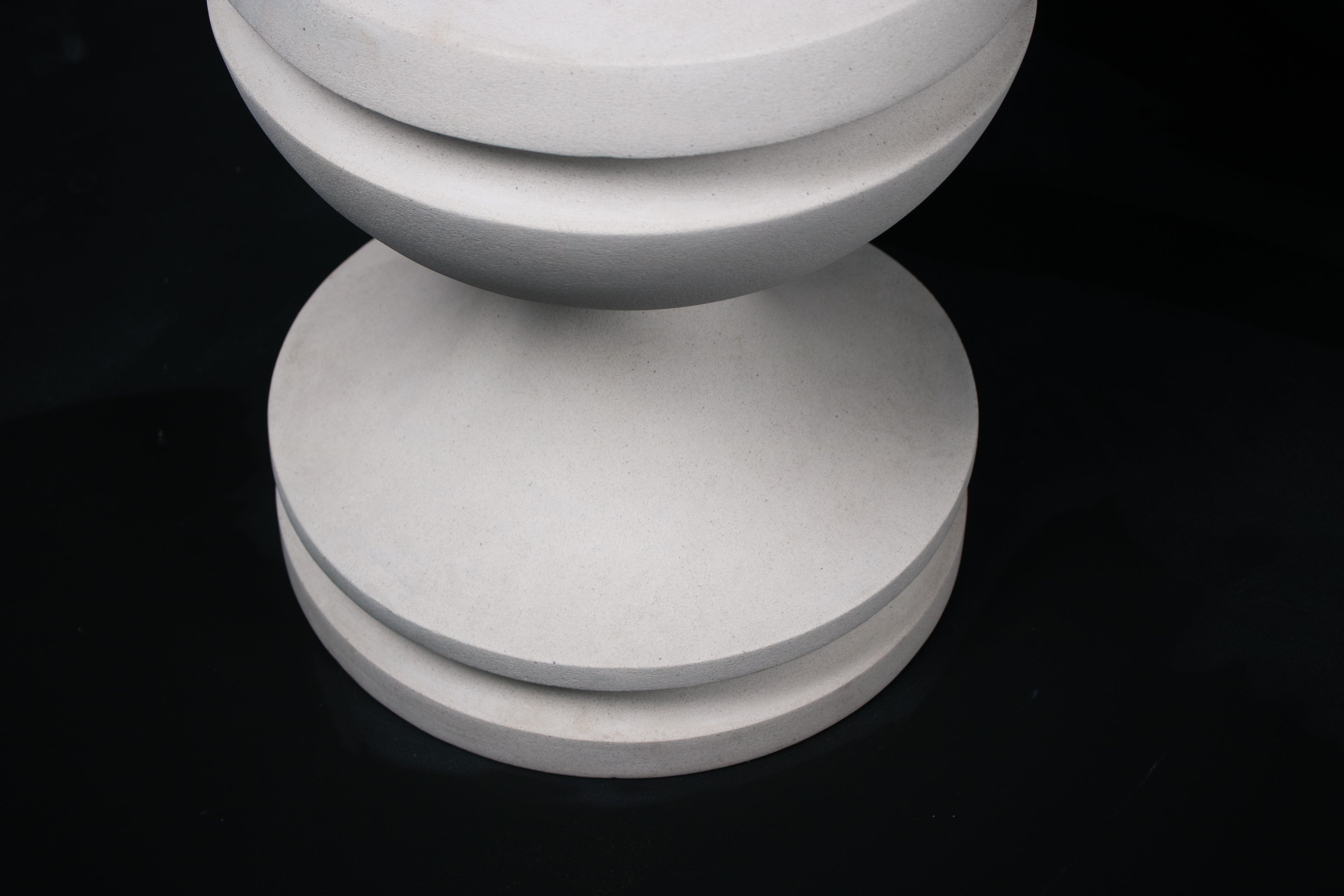 Chalice barstool in white. The substantial turned base draws on classical column and urn forms, a layered circular foot rises through a bulbous lower body, pinches to a narrow waist, then flares outward to support a round white bouclé upholstered seat.