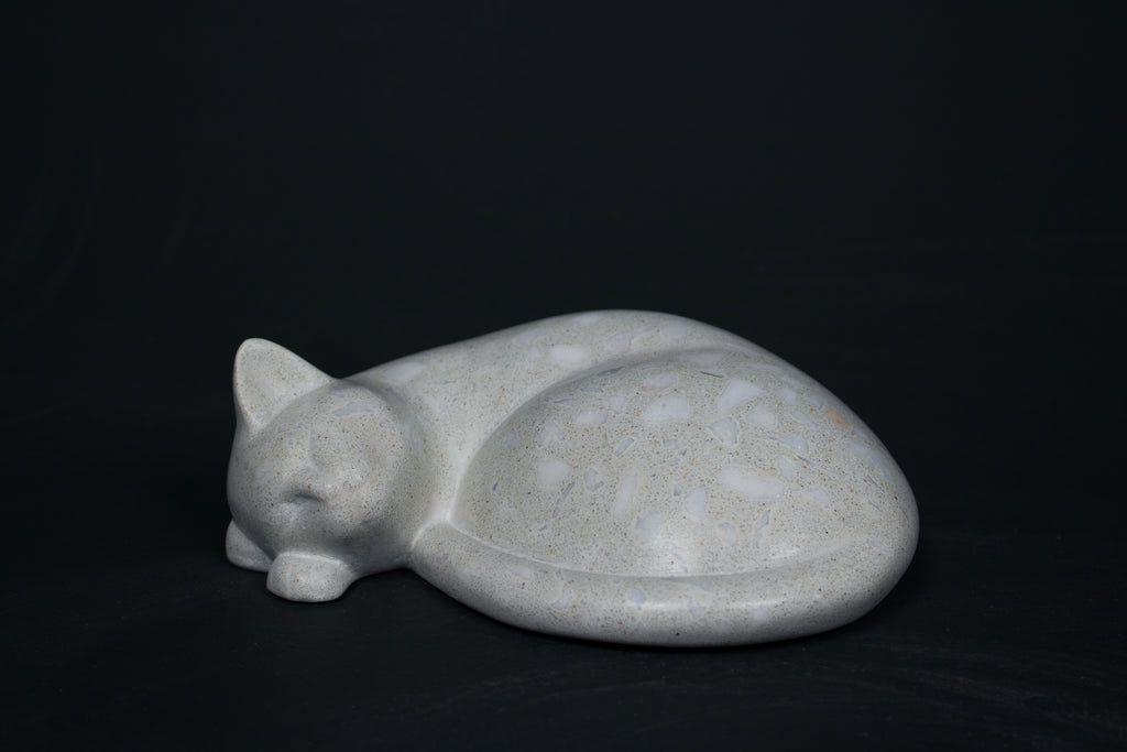 The Curly Cat terrazzo doorstop. A close-up view reveals the smoothly cast sleeping cat form, head resting on tucked paws, eyes closed, body curled into a low rounded mass. The pale grey terrazzo surface is flecked with irregular fragments of white and blush quartz.