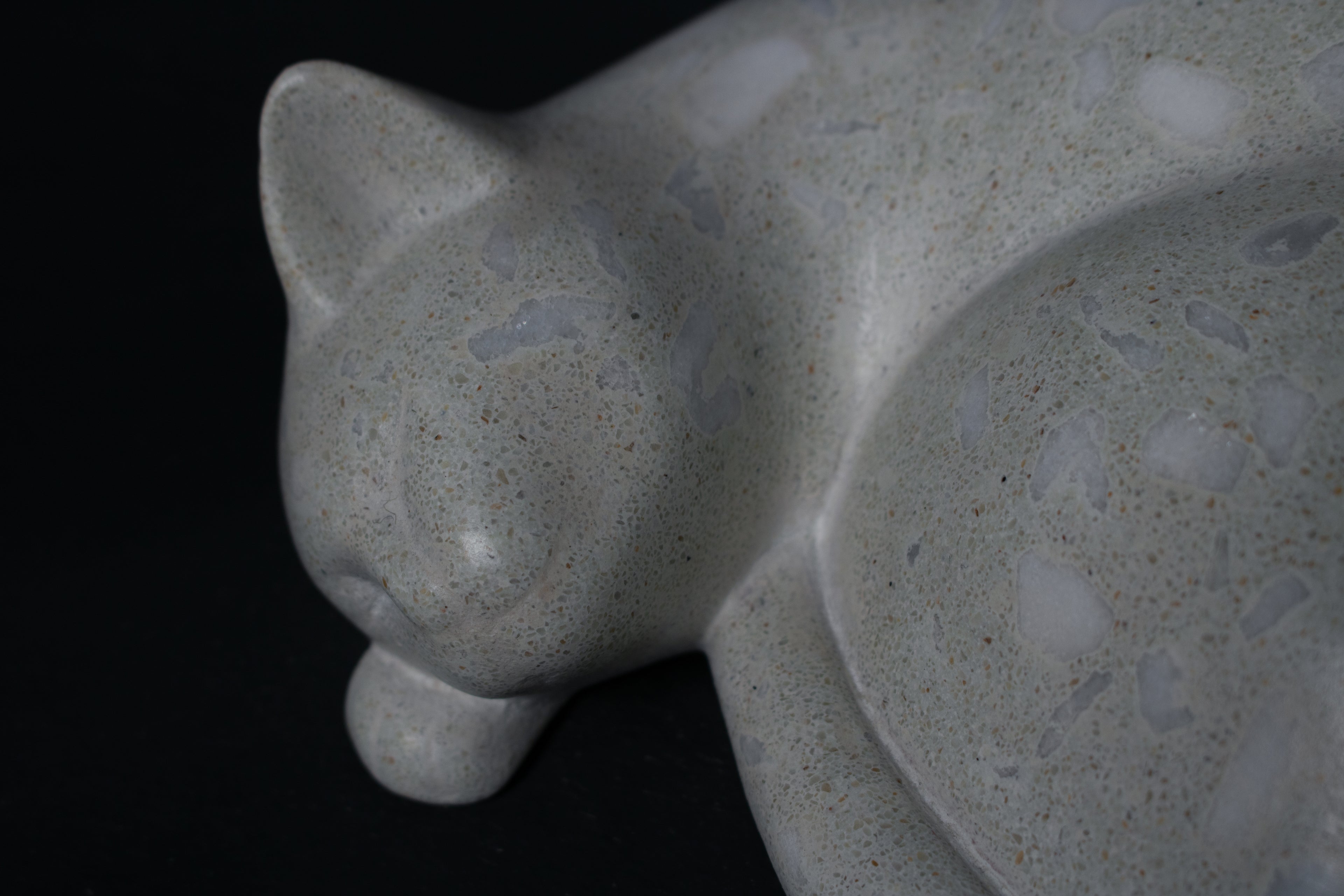 The Curly Cat terrazzo doorstop. A close-up view reveals the smoothly cast sleeping cat form, head resting on tucked paws, eyes closed, body curled into a low rounded mass. The pale grey terrazzo surface is flecked with irregular fragments of white and blush quartz.