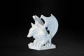 White plaster sculpture of a winged gargoyle in a crouching position on a base