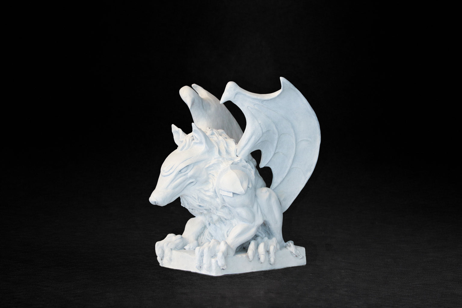 White plaster sculpture of a winged gargoyle in a crouching position on a base