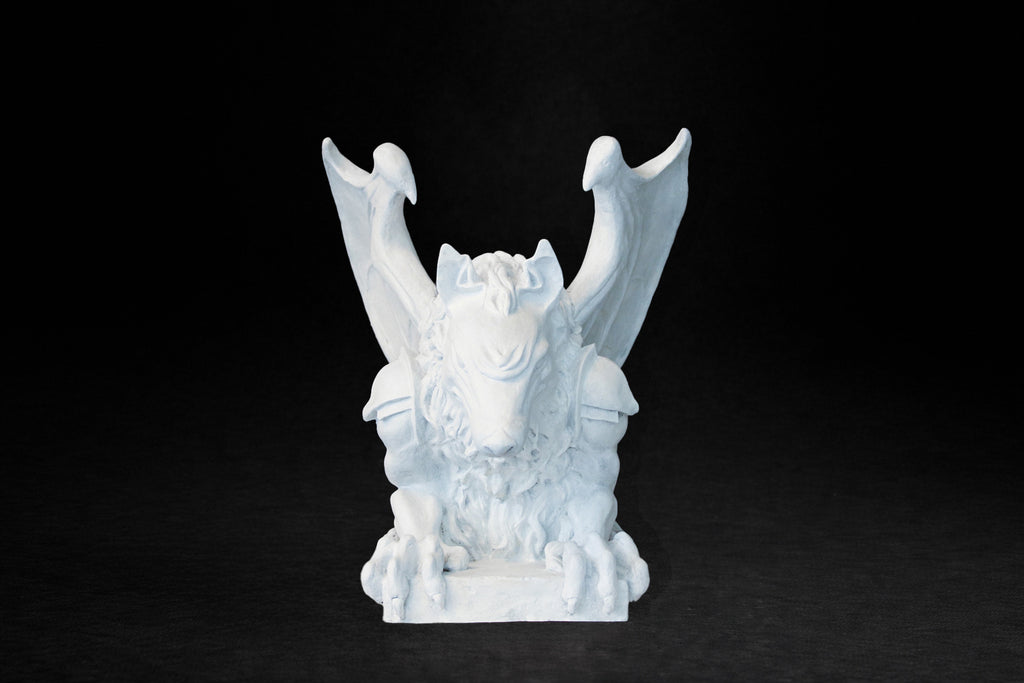 White plaster sculpture of a winged gargoyle in a crouching position on a base