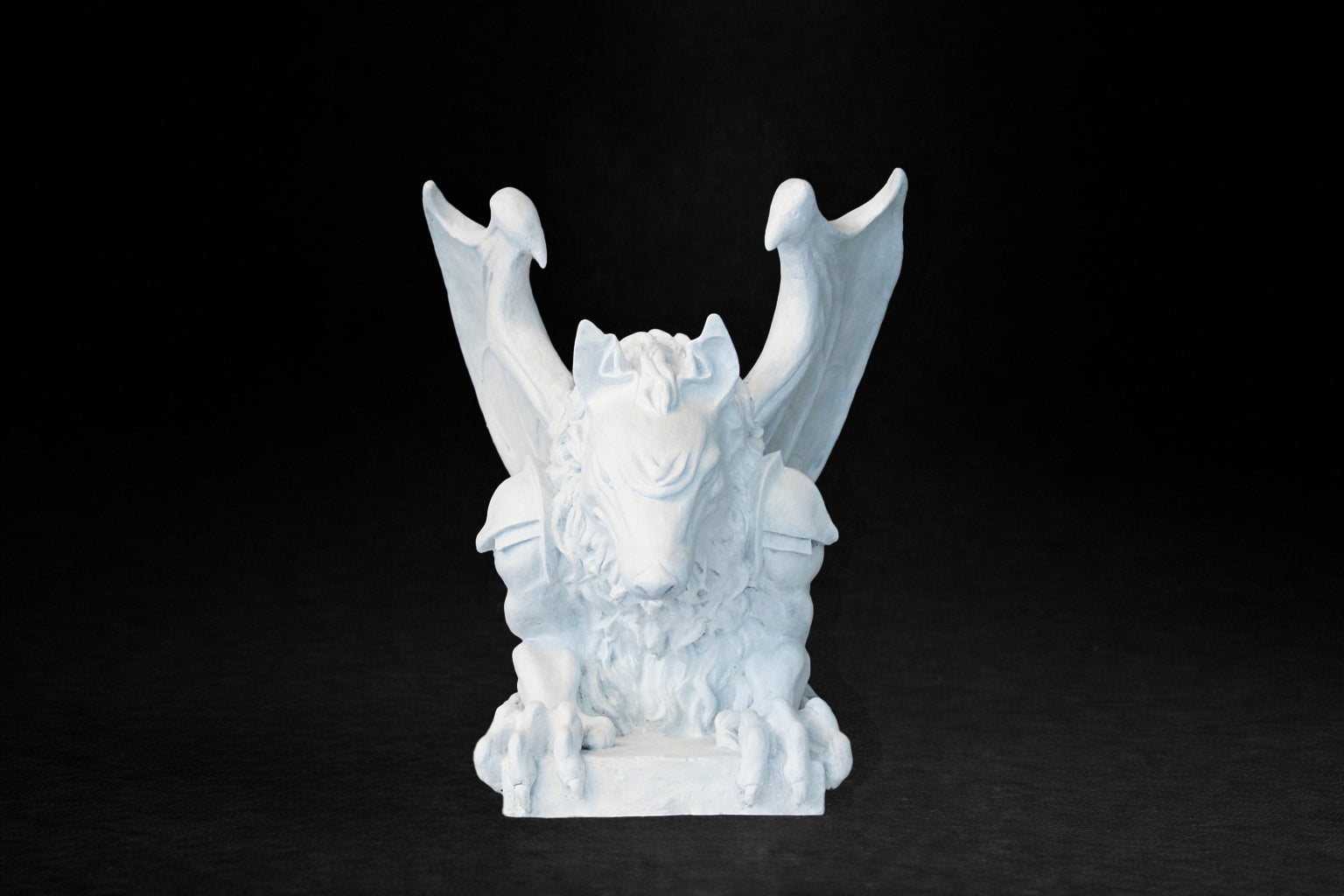 White plaster sculpture of a winged gargoyle in a crouching position on a base