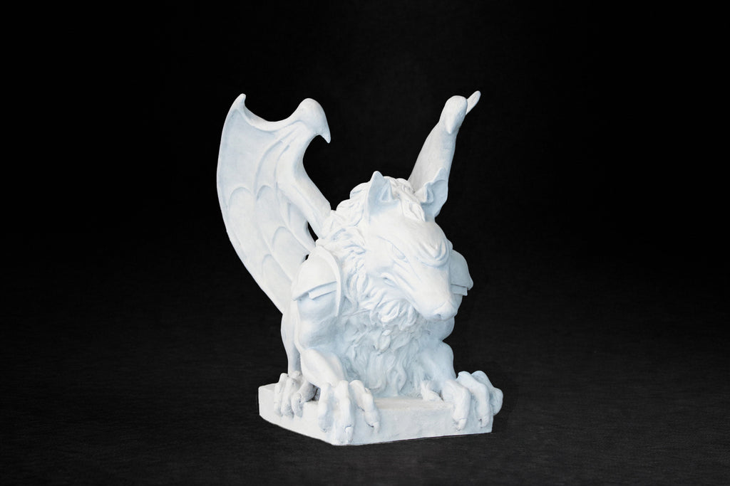 White plaster sculpture of a winged gargoyle in a crouching position on a base