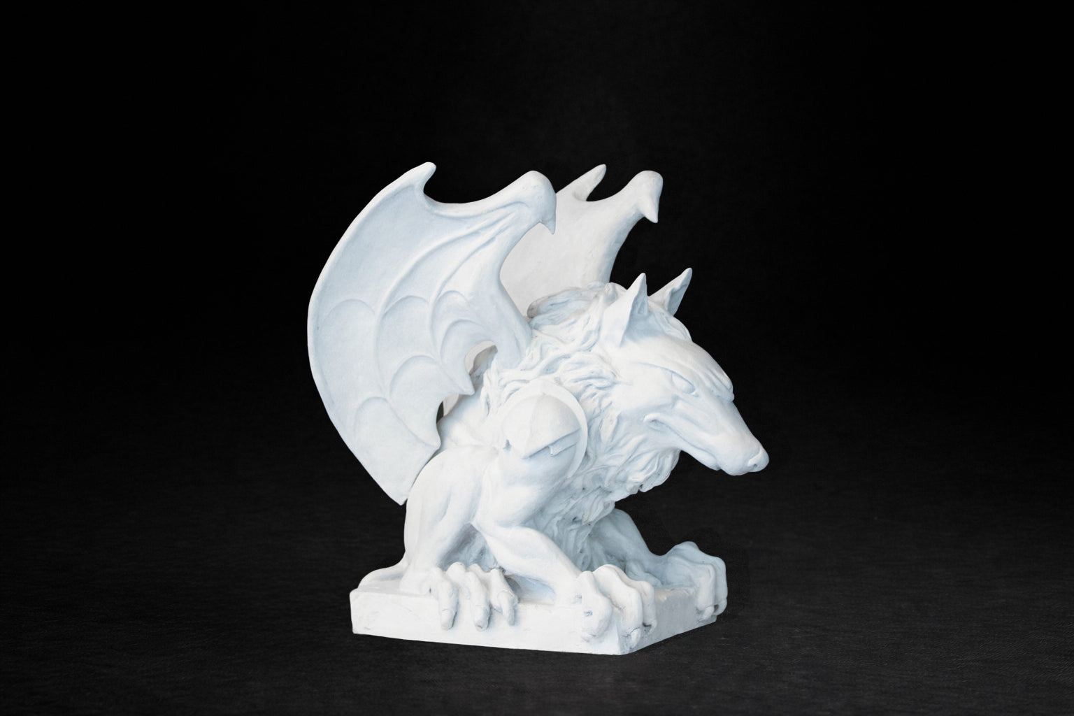 White plaster sculpture of a winged gargoyle in a crouching position on a base
