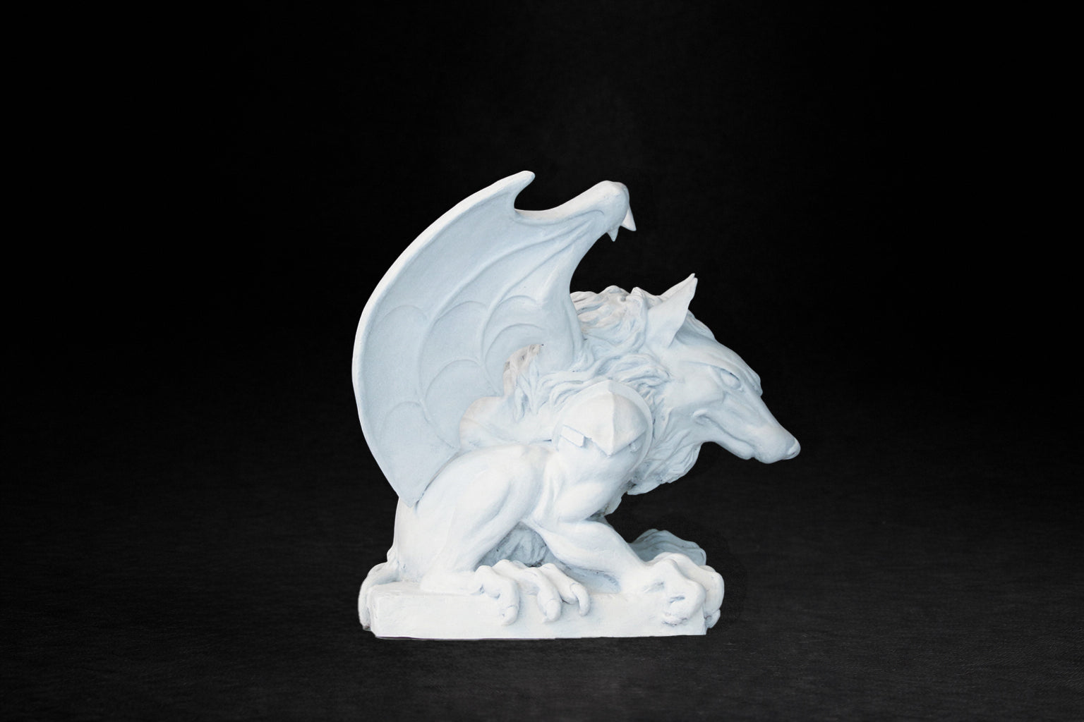 White plaster sculpture of a winged gargoyle in a crouching position on a base