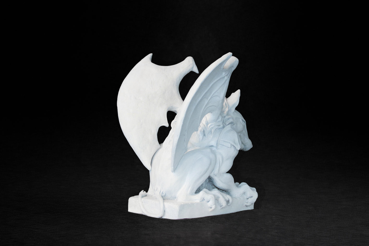 White plaster sculpture of a winged gargoyle in a crouching position on a base