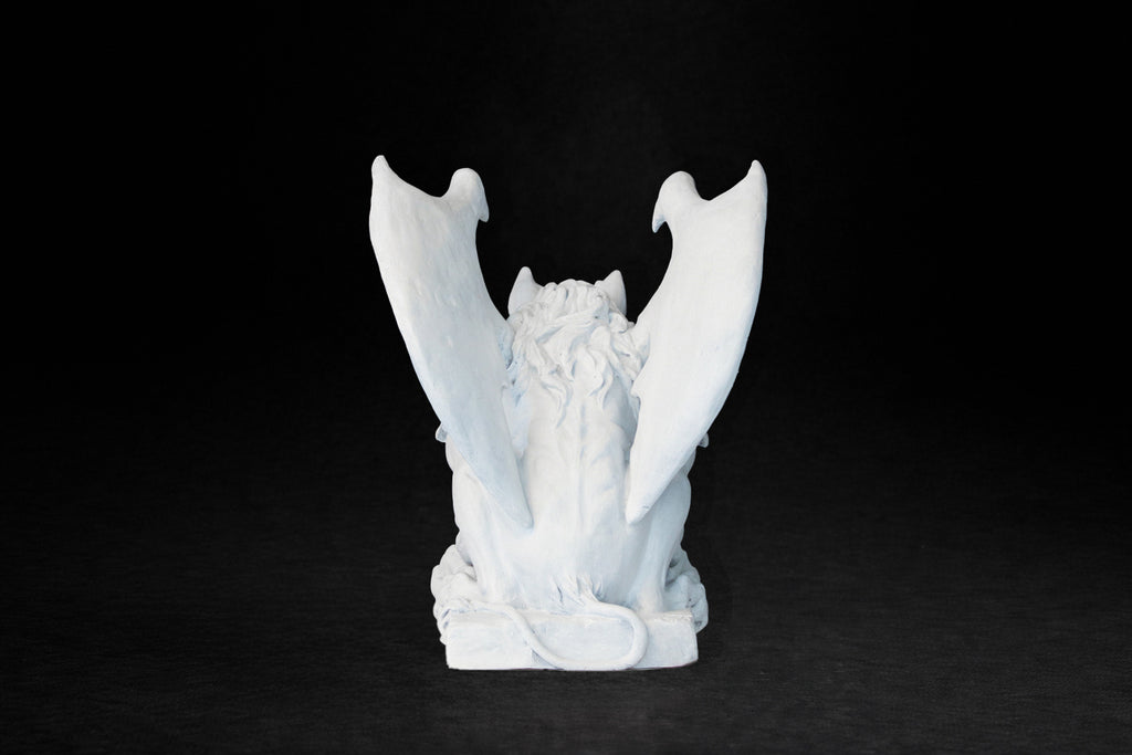 White plaster sculpture of a winged gargoyle in a crouching position on a base