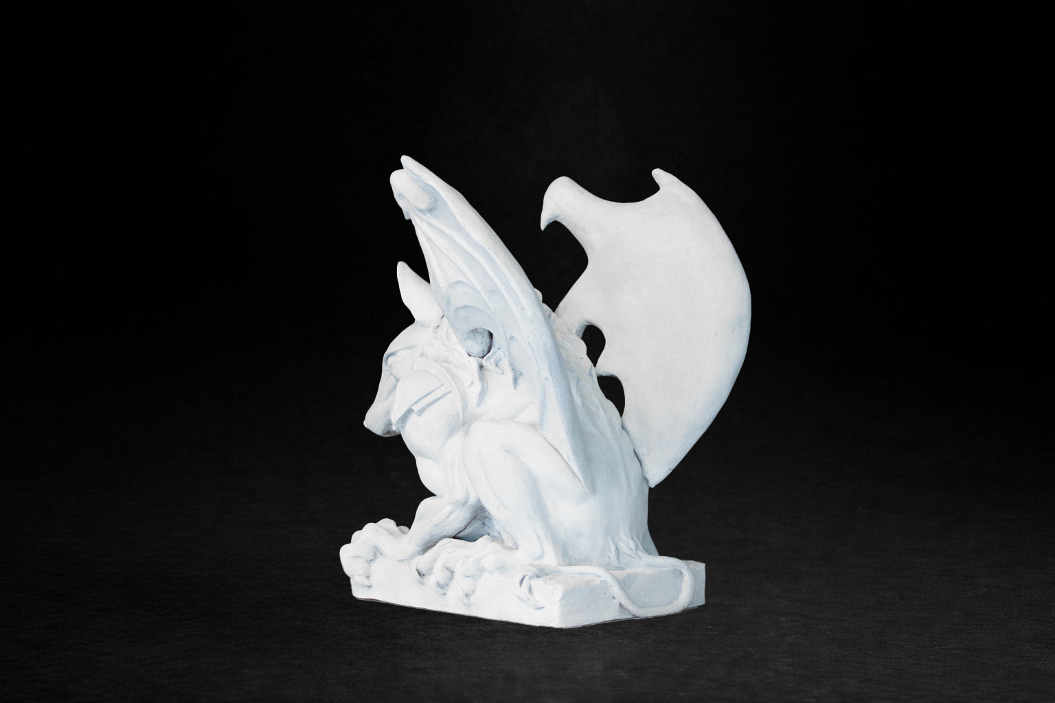 White plaster sculpture of a winged gargoyle in a crouching position on a base