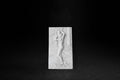 White plaster relief tile depicting a classical nude female figure carrying an urn within a columned architectural setting.
