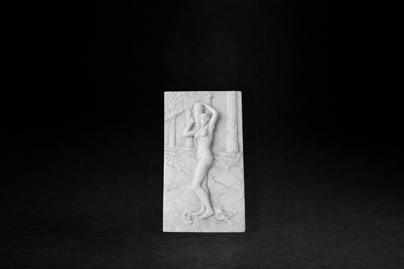 White plaster relief tile depicting a classical nude female figure carrying an urn within a columned architectural setting.