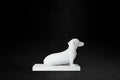White plaster sculpture of a seated dachshund on a rectangular base, gazing forward.