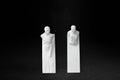 Two white plaster wall-mounted figural panels depicting elongated human forms emerging from vertical plaques.