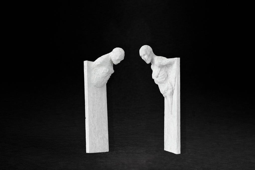 Two white plaster wall-mounted figural panels depicting elongated human forms emerging from vertical plaques.