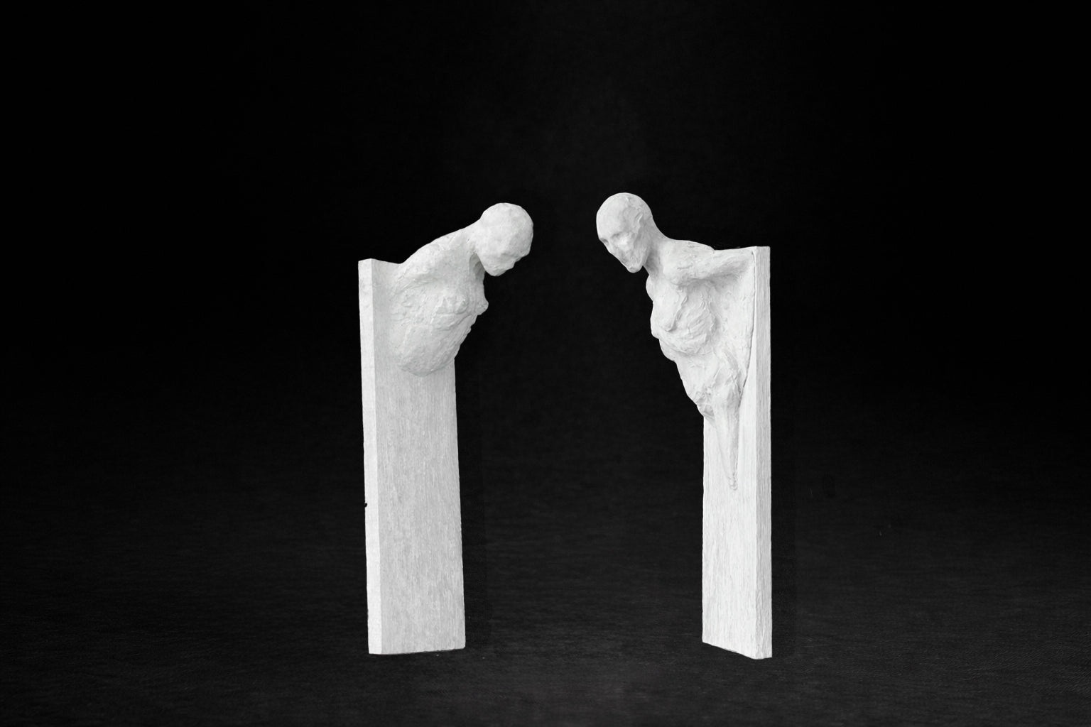 Two white plaster wall-mounted figural panels depicting elongated human forms emerging from vertical plaques.