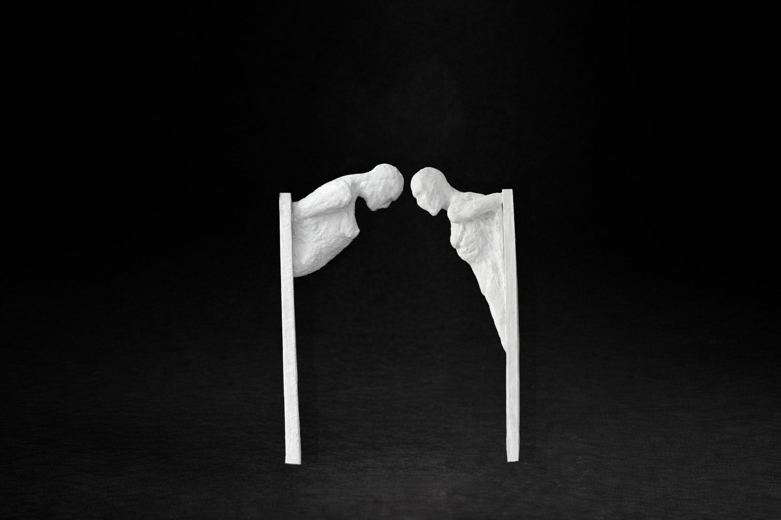 Two white plaster wall-mounted figural panels depicting elongated human forms emerging from vertical plaques.