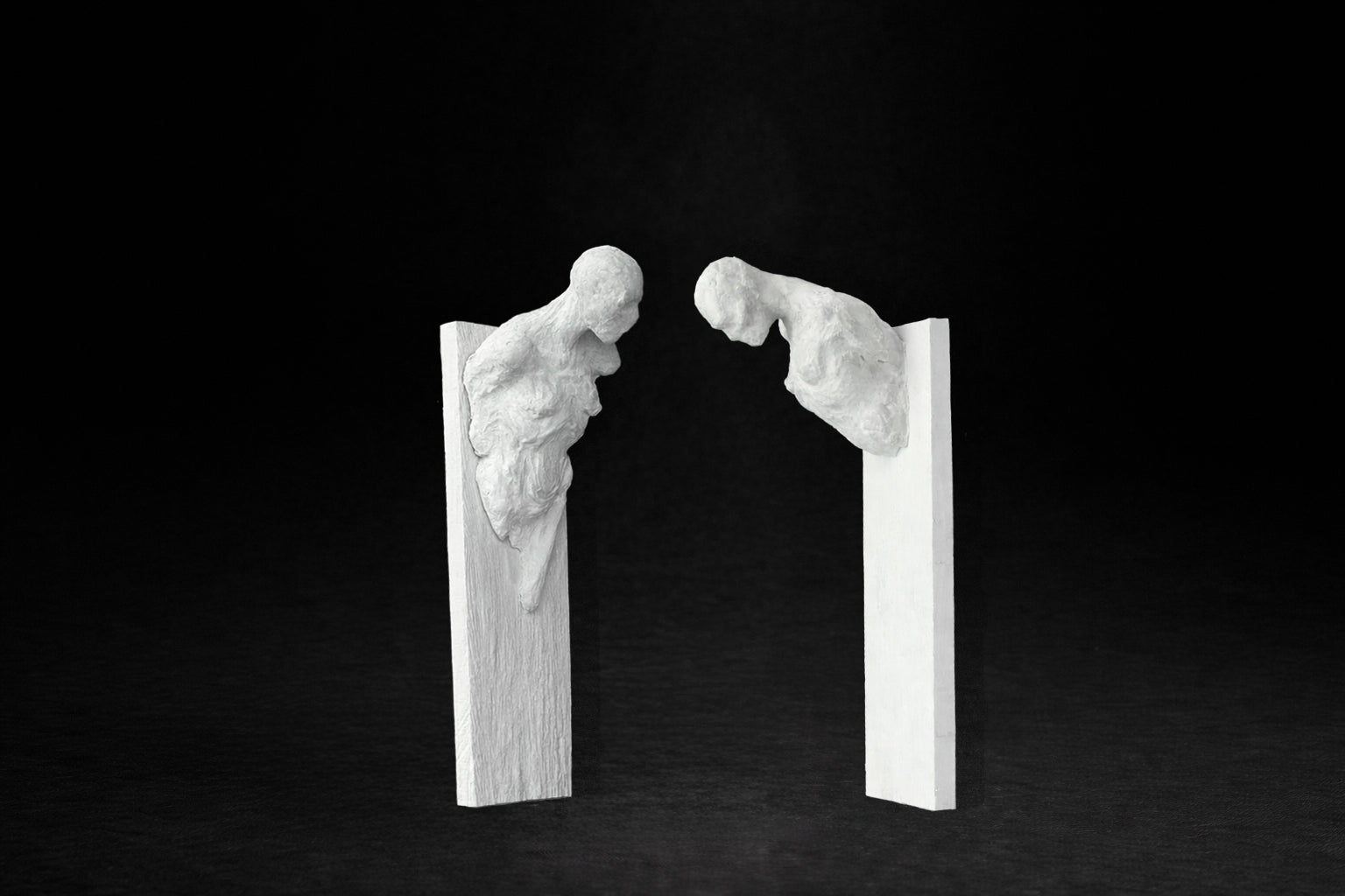Two white plaster wall-mounted figural panels depicting elongated human forms emerging from vertical plaques.
