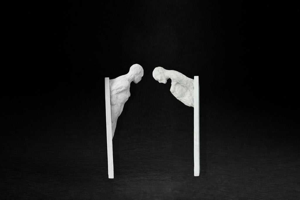 Two white plaster wall-mounted figural panels depicting elongated human forms emerging from vertical plaques.