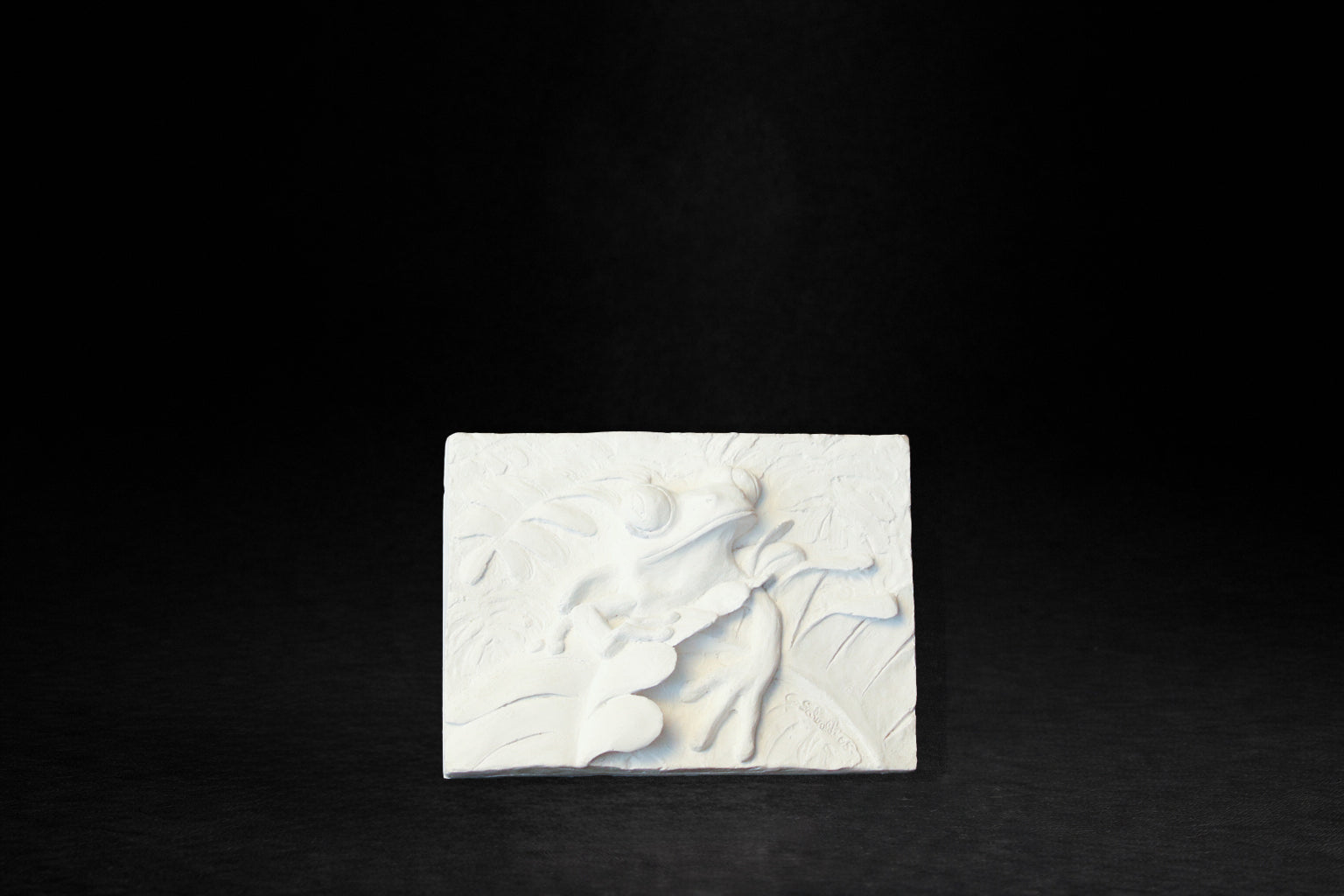 White plaster relief tile depicting a red-eyed tree frog among tropical vegetation.