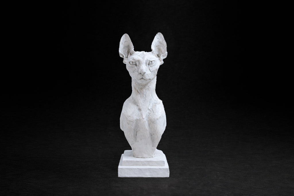 White plaster portrait bust of a Sphinx cat on a stepped square plinth.