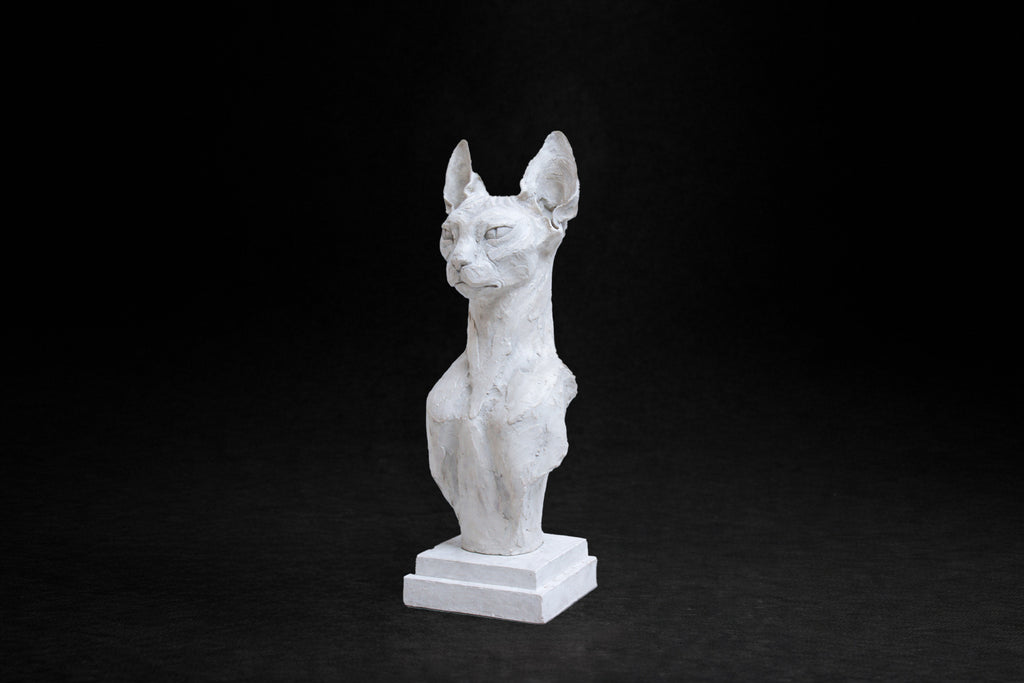 White plaster portrait bust of a Sphinx cat on a stepped square plinth.