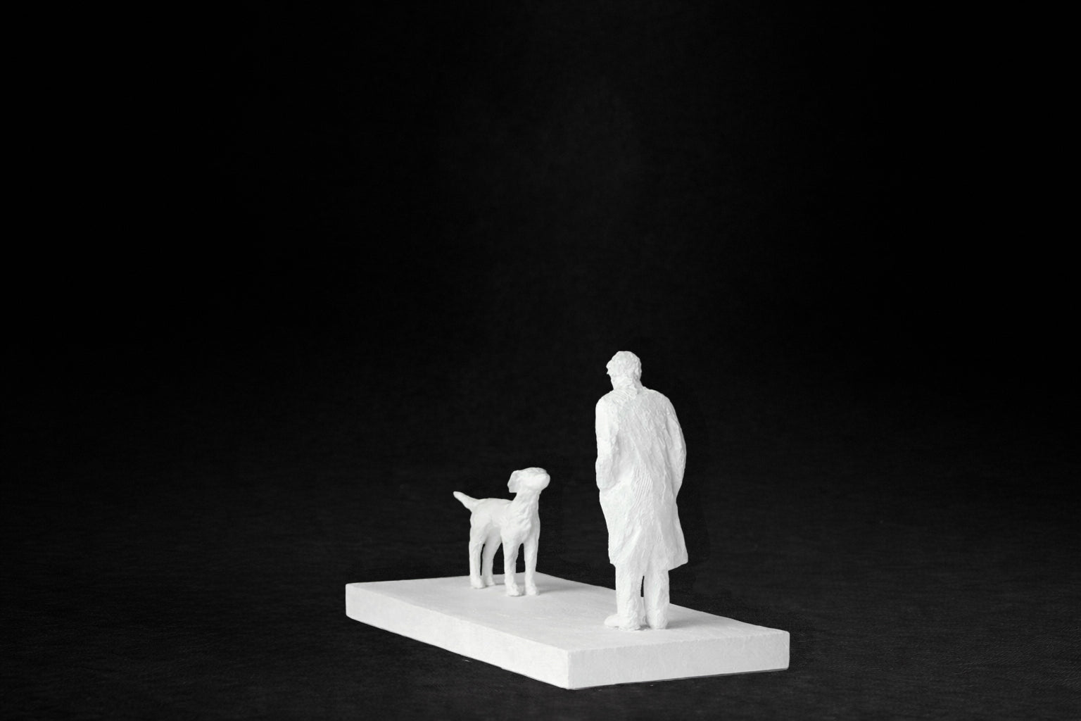 White plaster sculpture of a person and a dog facing each other on a rectangular base.