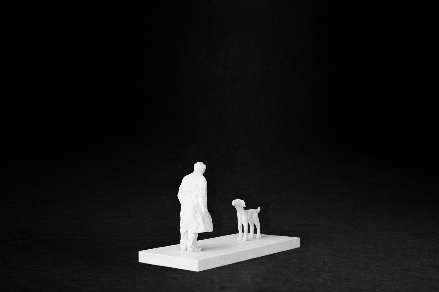 White plaster sculpture of a person and a dog facing each other on a rectangular base.