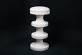 The Tambour barstool in white. The sculptural pedestal base features three stacked hourglass tiers that widen and narrow in alternating rhythm, topped with a round white bouclé upholstered seat.