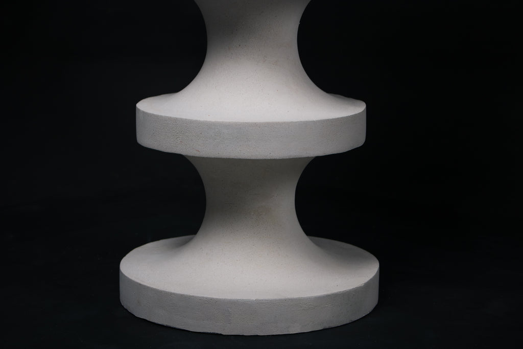 The Tambour barstool in white. The sculptural pedestal base features three stacked hourglass tiers that widen and narrow in alternating rhythm, topped with a round white bouclé upholstered seat.