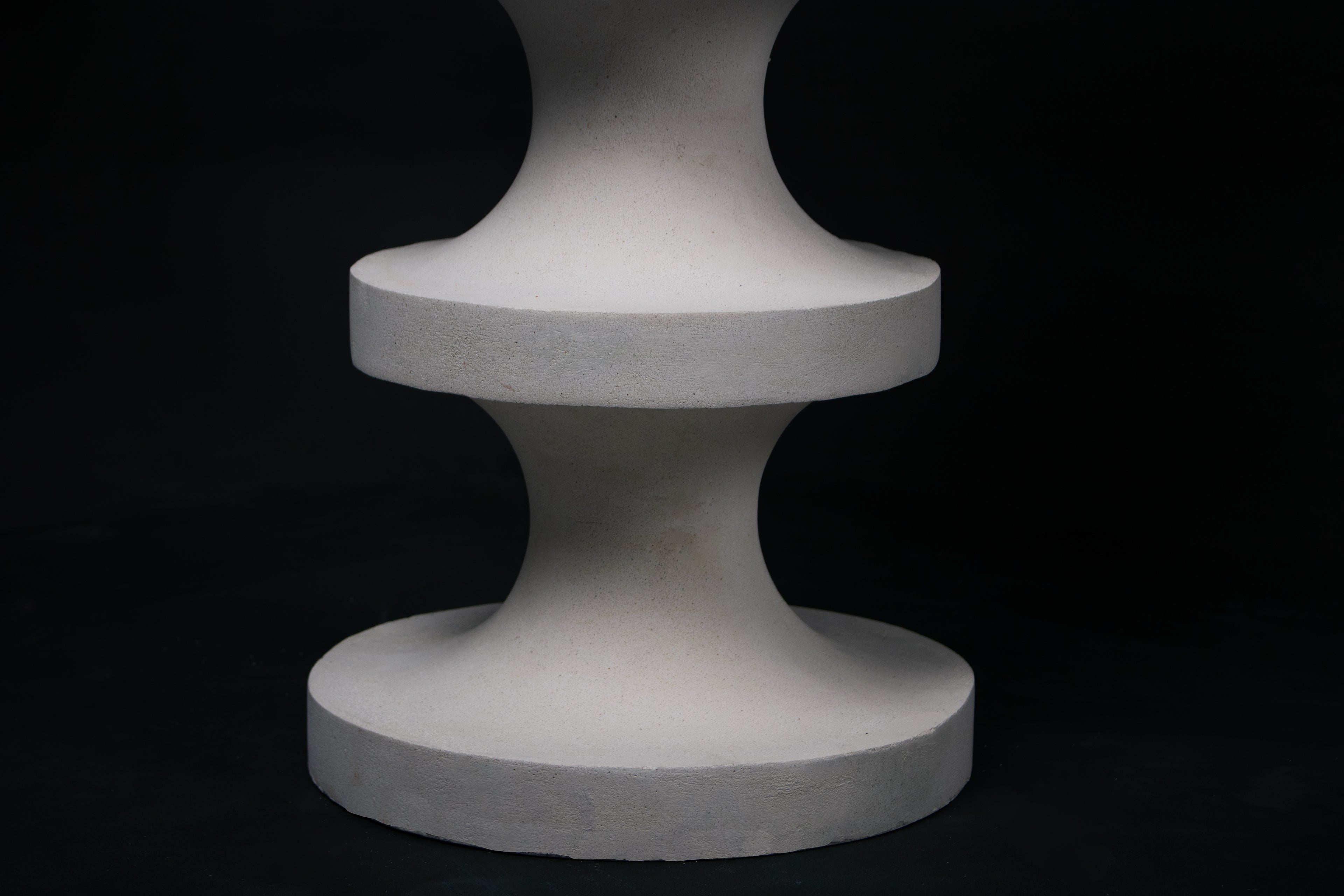 The Tambour barstool in white. The sculptural pedestal base features three stacked hourglass tiers that widen and narrow in alternating rhythm, topped with a round white bouclé upholstered seat.