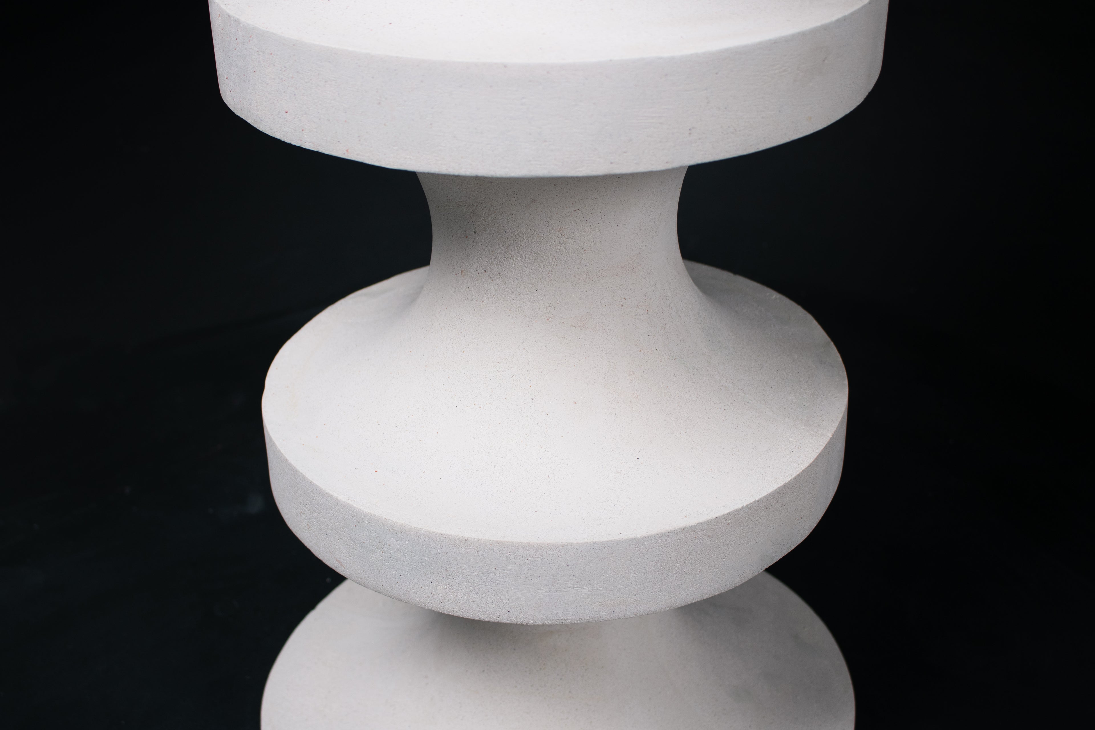 The Tambour barstool in white. The sculptural pedestal base features three stacked hourglass tiers that widen and narrow in alternating rhythm, topped with a round white bouclé upholstered seat.
