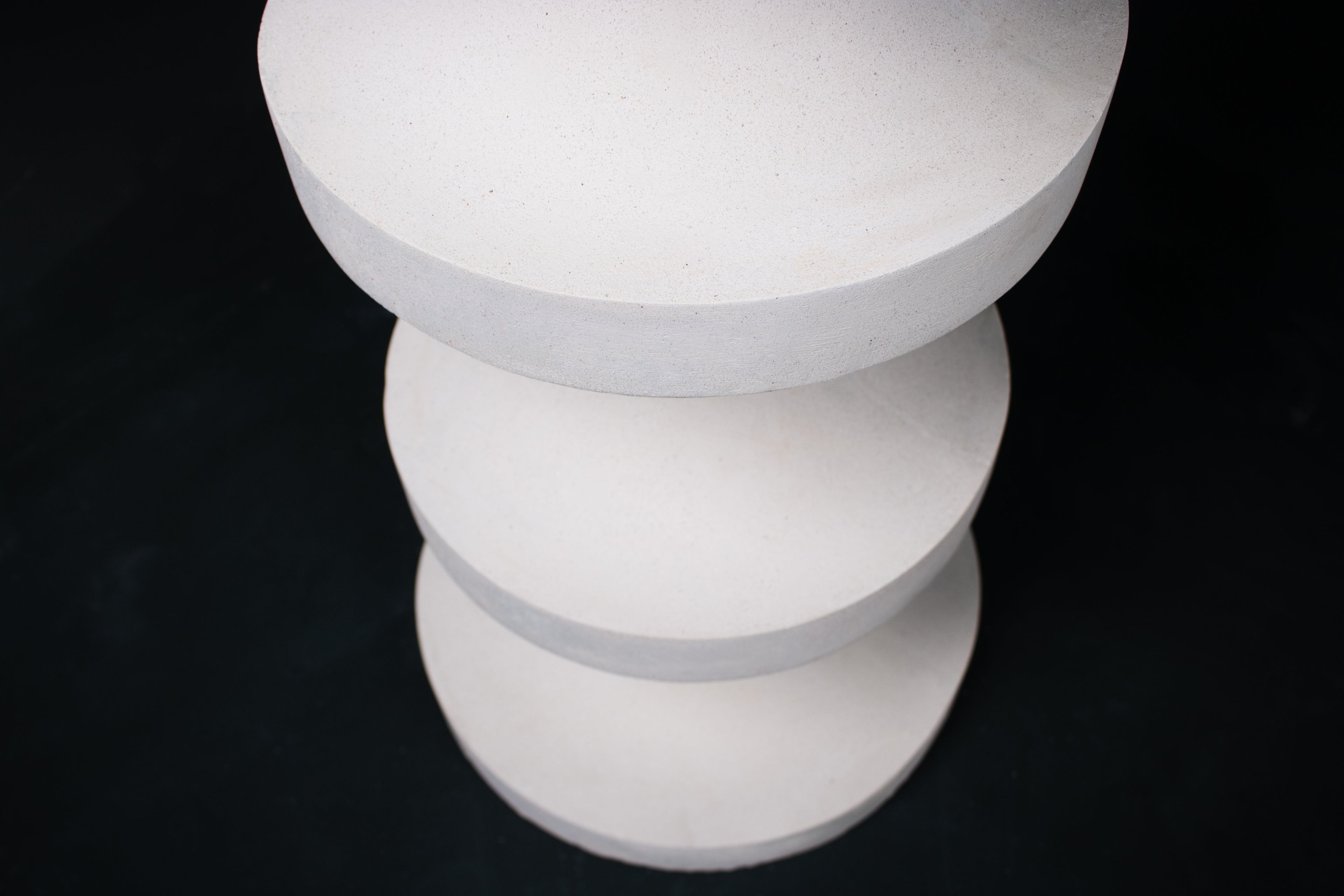 The Tambour barstool in white. The sculptural pedestal base features three stacked hourglass tiers that widen and narrow in alternating rhythm, topped with a round white bouclé upholstered seat.